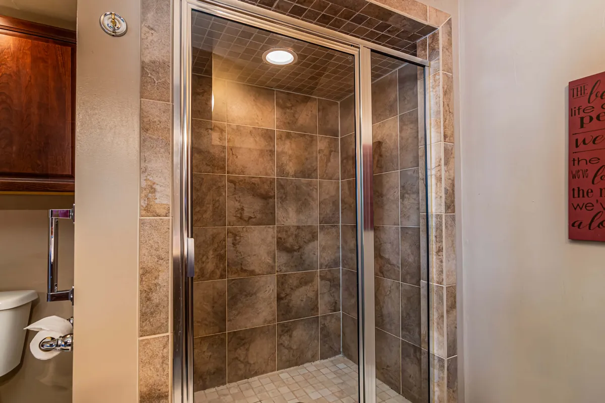A modern ensuite bathroom with a glass shower enclosure, textured tiles, and decorative wall art, evoking a spa-like experience perfect for daily routines and relaxation.