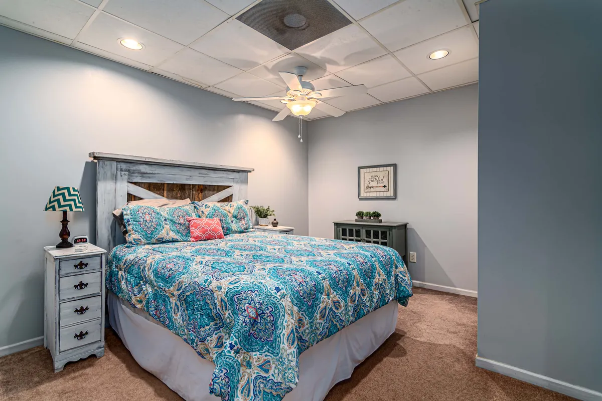 A bedroom with a king bed adorned in colorful bedding, complemented by a nightstand and ceiling fan. Natural light streams through the windows, creating a welcoming and restful ambiance ideal for relaxation.