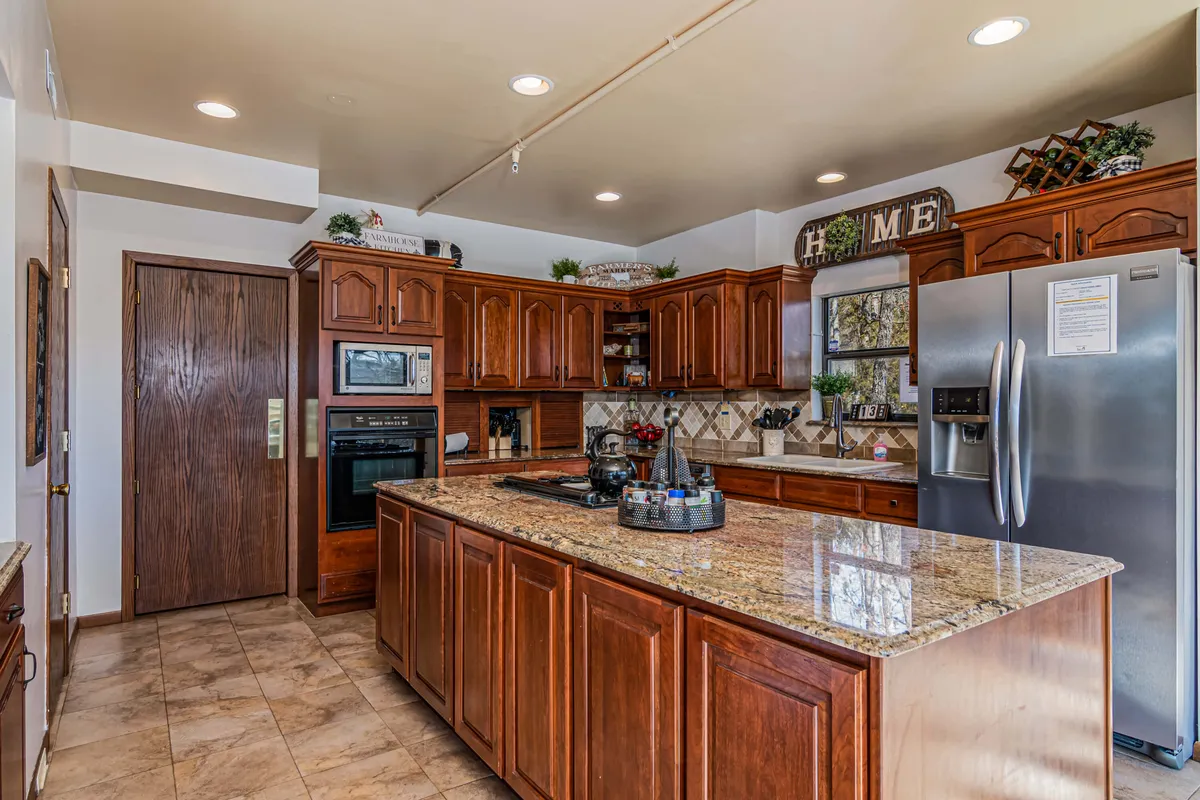 A modern, fully equipped kitchen with granite countertops, stainless steel refrigerator, warm wooden cabinetry, and decorative accents, inviting guests to cook, converse, and create meals together.