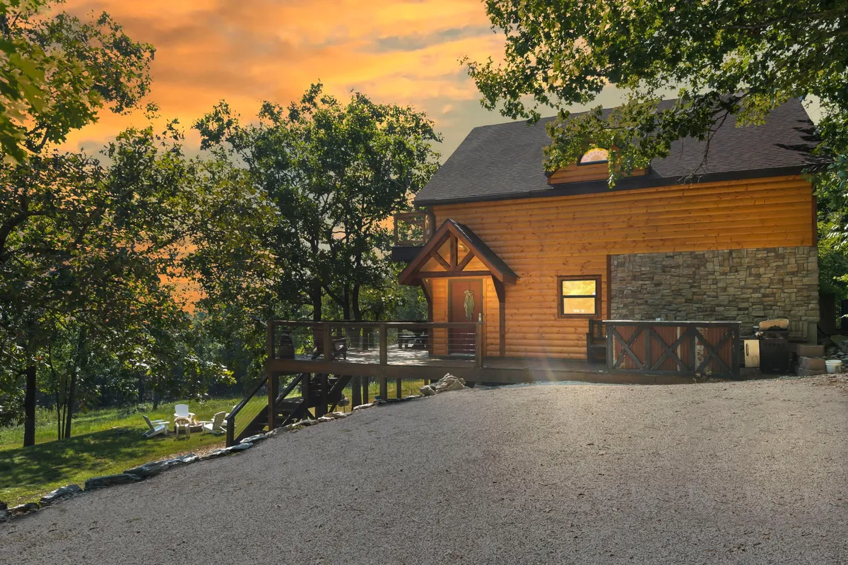 This image captures the exterior of a wooden house with a spacious deck, surrounded by lush trees and set against a stunning sunset sky. The inviting deck offers space for relaxation, socializing, and enjoying the outdoors, while the tranquil natural setting hints at nearby trails and nature exploration.