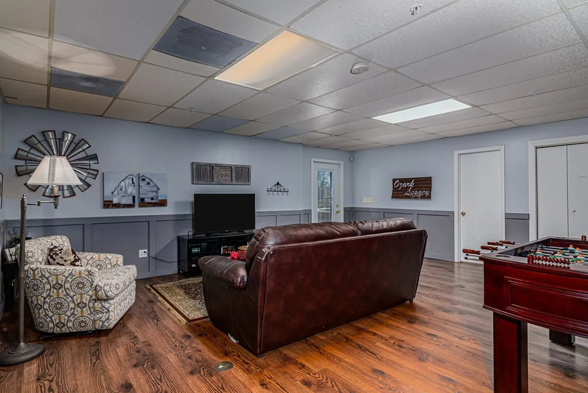 A secondary living area featuring a leather sofa, media center with TV, foosball table, decorative armchair, and wall art. The layout encourages family gatherings, movie nights, and playful competitions in a relaxed environment.