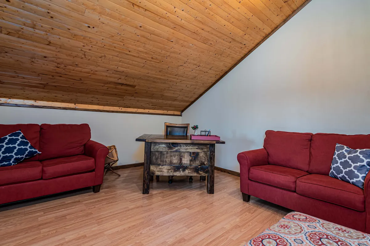 A cozy office nook featuring red sofas, a wooden desk, and decorative cushions. The space is both inviting and functional, ideal for quiet work or reading.