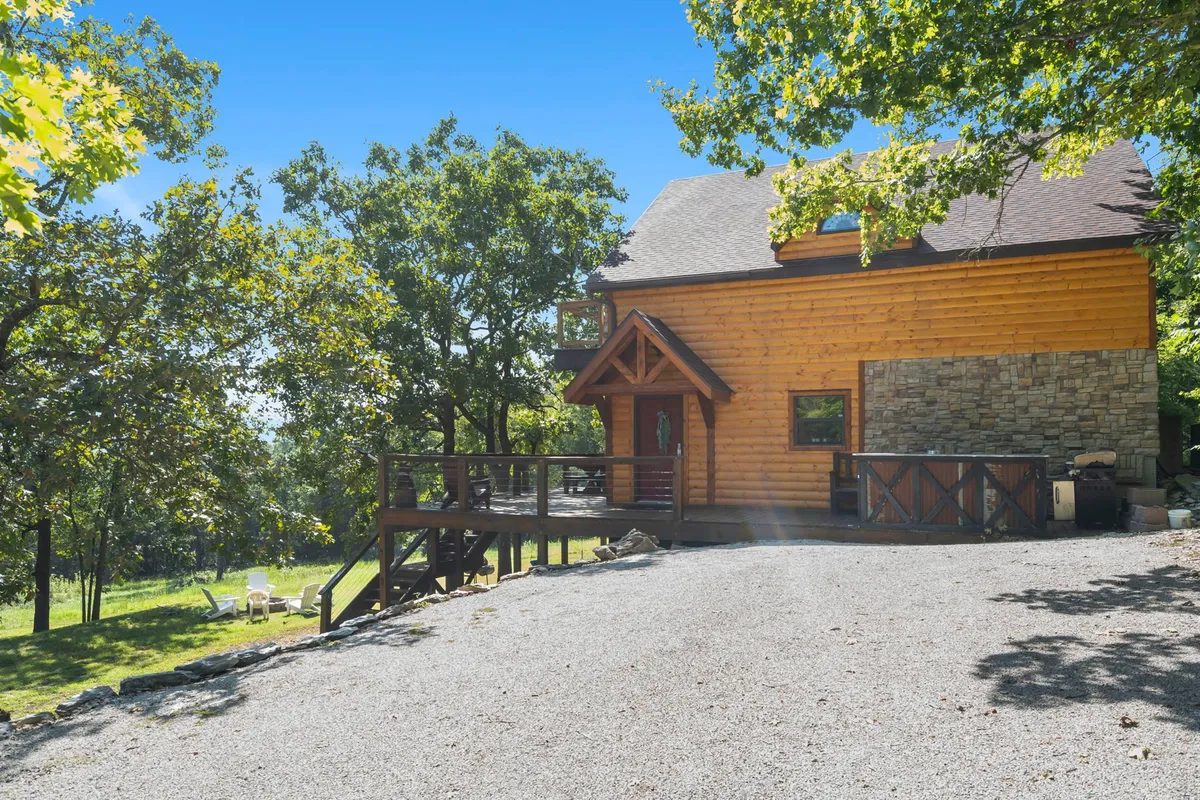An exterior view of a wooden home with stone accents and a spacious deck area, set amid natural surroundings. The deck beckons for gatherings, while the house blends beautifully into its serene environment.