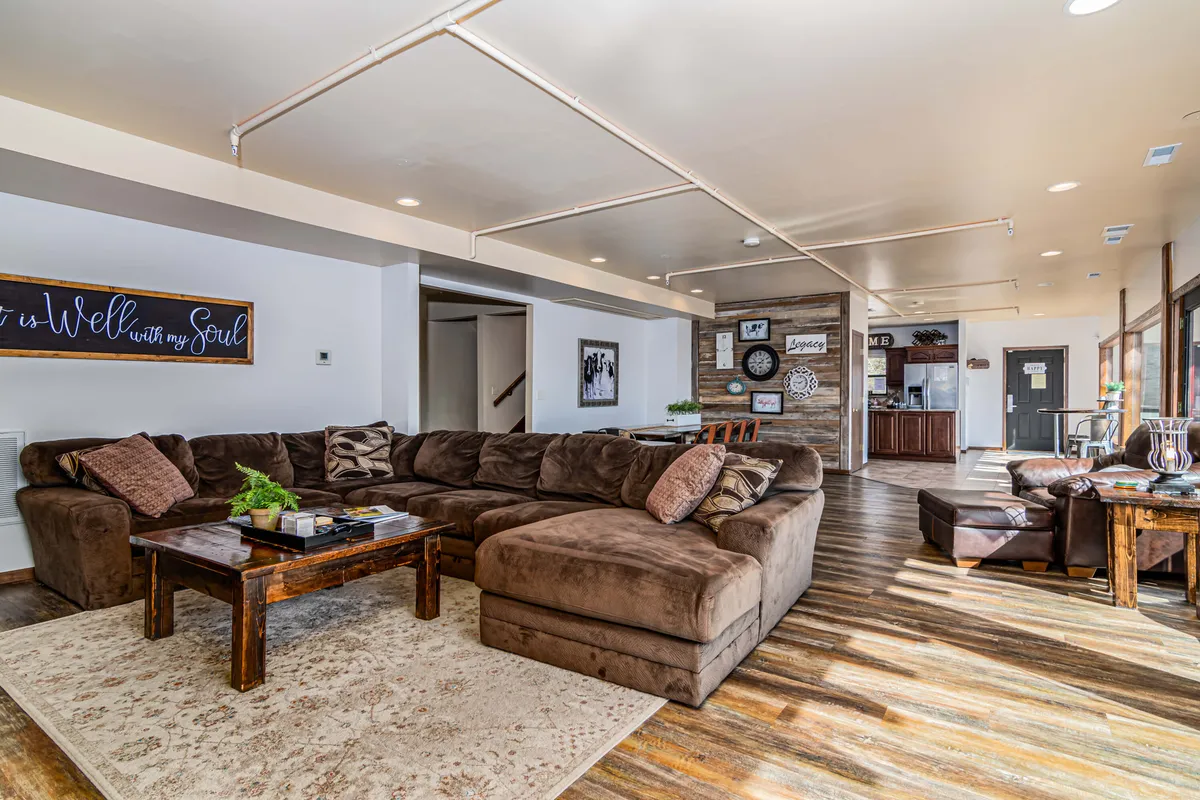 This interior scene displays a large sectional sofa, a wooden coffee table, decorative wall art, and a view into the kitchen area. The open, comfortable space is designed for group relaxation, movie nights, and intimate gatherings after a day out.