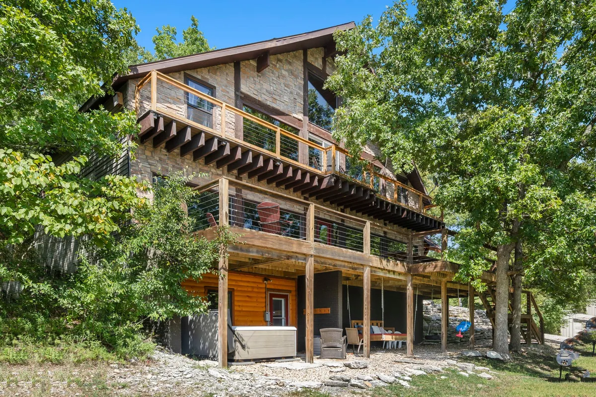 A peaceful view of the multi-level wooden deck surrounded by trees, featuring a hot tub and ample space for relaxing or socializing. The tranquil backdrop highlights the property's seclusion and its opportunities for stargazing and unwinding after a day of play.