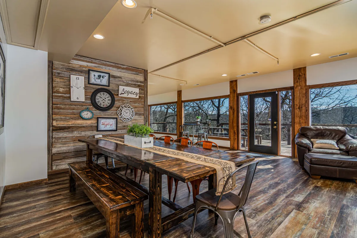 A spacious, rustic dining room with a large wooden table set for a group, rustic wall décor, and large windows that fill the room with natural light and offer sweeping views of the outdoors. The scene is set for communal meals and memorable gatherings.