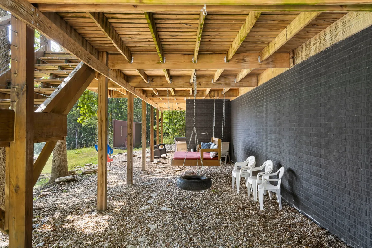 An outdoor seating area with a playful tire swing hanging from a wooden structure and white chairs set up for relaxation. The area is enveloped in lush greenery, offering both fun for kids and relaxation for adults.