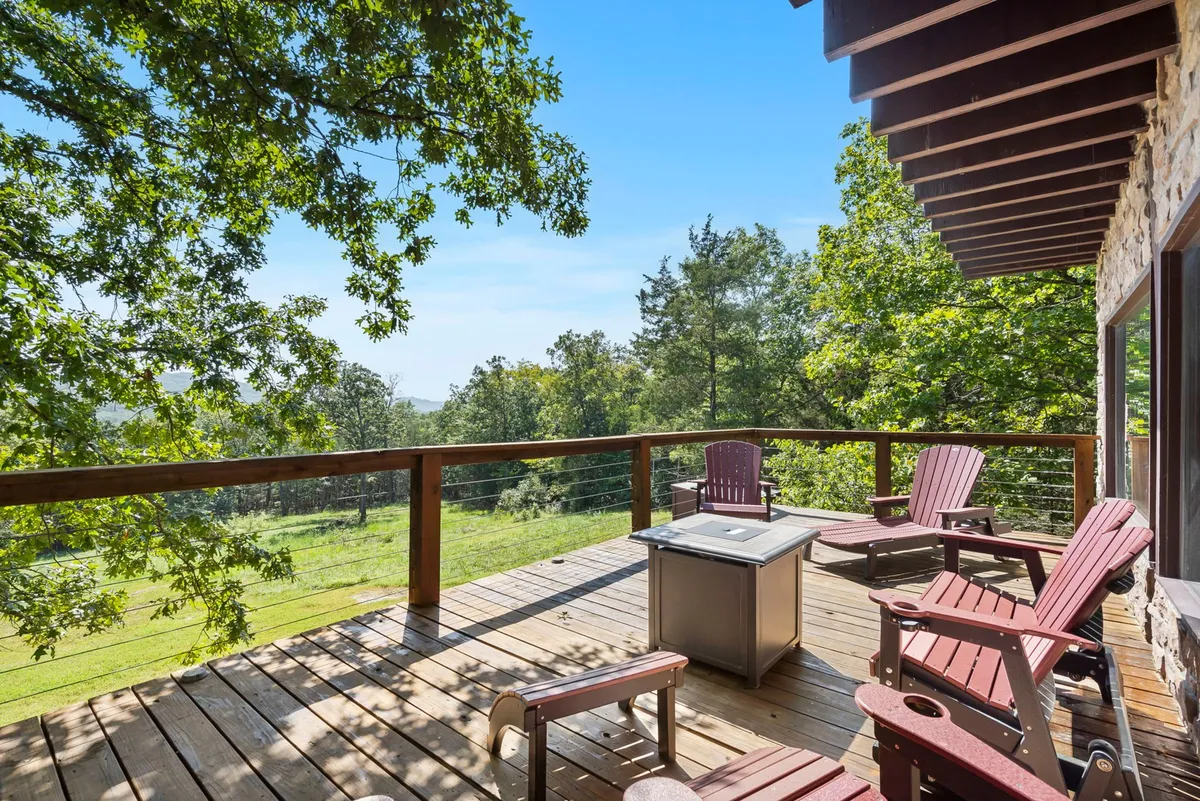 A broad wooden deck lined with Adirondack chairs faces a tranquil landscape of rolling hills and tall trees. The central fire pit is set up as the perfect spot for evening gatherings while the surrounding natural setting invites relaxation and screen-free moments.