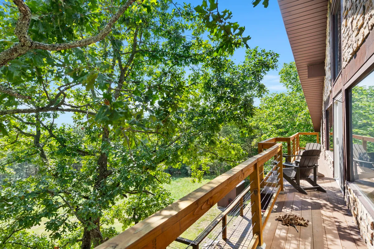 A wooden deck featuring Adirondack chairs, surrounded by lush greenery. The inviting setup suggests a peaceful spot for birdwatching, reading, or enjoying the stars at night.