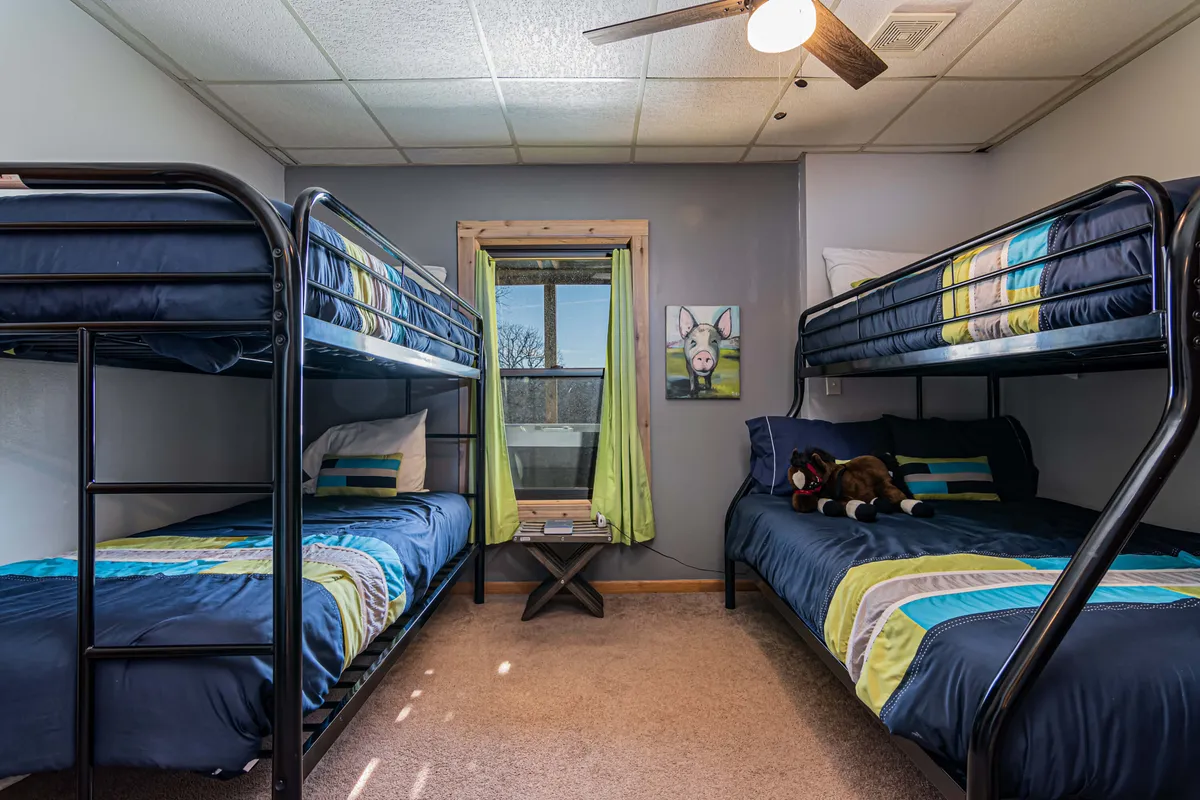 A cheerful bunk room with bunk beds featuring colorful bedding, light curtains allowing in natural light, playful wall art, and an overall sense of coziness and vibrancy. The room is designed to accommodate multiple children or guests and invites sleepovers and playful gatherings.